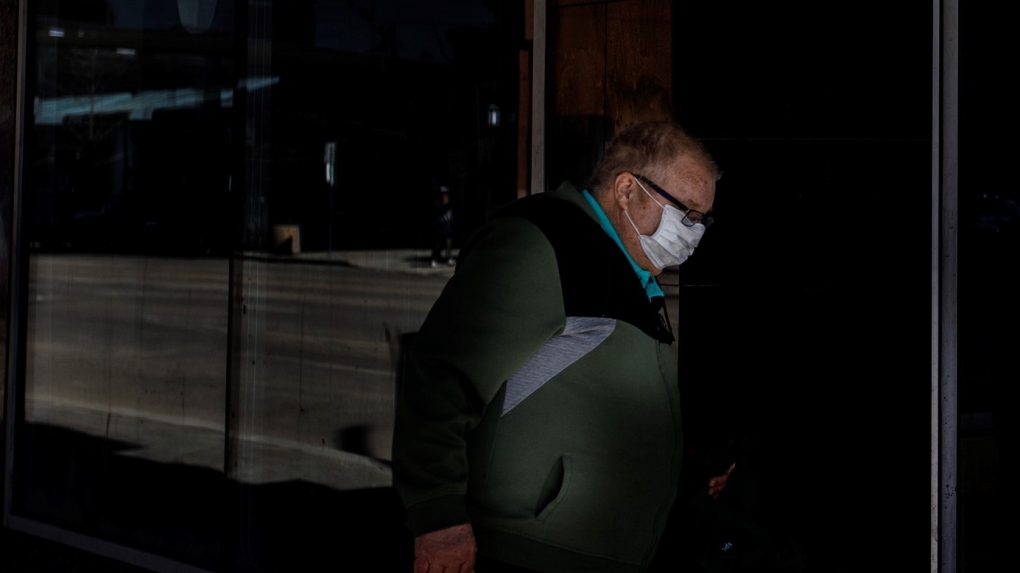 A person walks through a spot of light while wearing a mask to help the stop of COVID-19 during the world pandemic, in Edmonton Alta, on Wednesday April 8, 2020. THE CANADIAN PRESS/Jason Franson